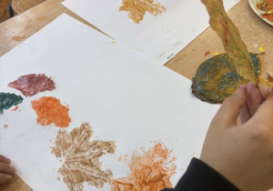 Dziecko odbija na białej kartce liścia zamoczonego w farbie.