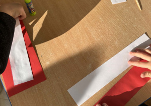 Dzieci przy stoliku wykonują flagę Polski z wyciętych elementów.