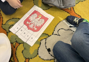Dzieci z pociętych puzzli układają napis i obrazek- Godło Polski.