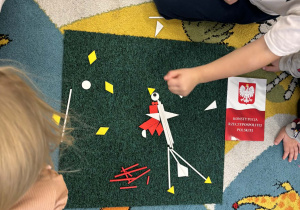 Dzieci na dywanie układają z darów Froebla Godło Polski.