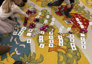 Dzieci na dywanie układają i dopasowują liczbę bombek do cyfr.