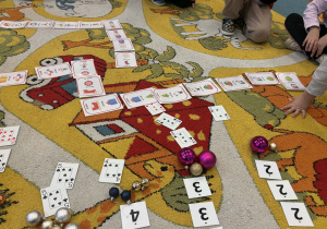 Dzieci na dywanie układają karty do zabawy - ja mam, kto ma.