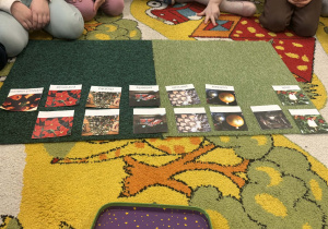 Dzieci siedzą na dywanie, a przed nimi karty z symbolami świątecznymi.