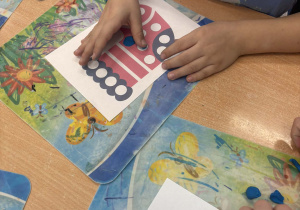 Dzieci przy stoliku wylepiają z plasteliny skarpetę.