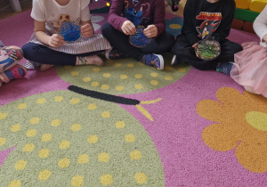 Dzieci siedzą przed choinką i prezentują swoje sensoryczne bombki.