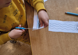 Chłopiec tnie nożyczkami fryzurę na kartce papieru.