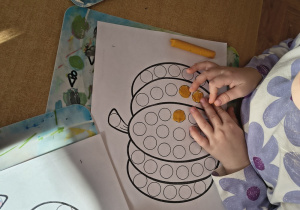 Dziewczynka wykleja plasteliną dynię.