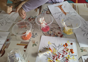 Dzieci malują patyczkami kosmetycznymi listki na drzewie.