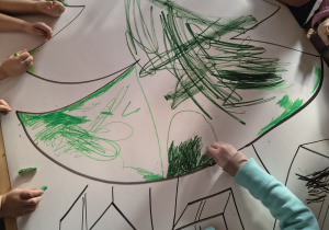 Dzieci kolorują na zielono choinkę.