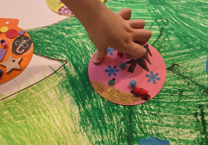 Dziecko przykleja swoją udekorowaną bombkę na choinkę.