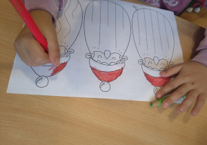 Dziewczynka koloruję czapkę Mikołajowi.