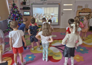 Dzieci naśladują ruchy przedstawione na tablicy multimedialnej.