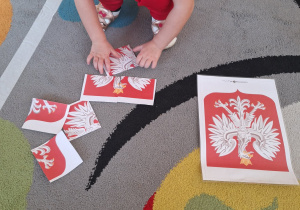 Dziewczynka układa Godło Polski z wyciętych elementów.