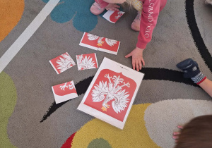 Dziewczynka układa Godło Polski z puzzli na dywanie.