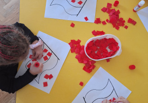 Dzieci przyklejają czerwoną bibułę na kontur flagi Polski.