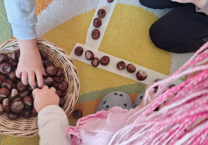 Dzieci układają z kasztanów trójkąt na dywanie.