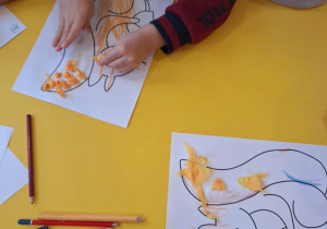 Chłopiec przykleja pomarańczową bibułę na ogon wiewiórki.