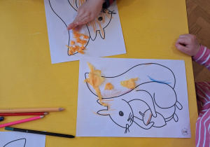 Dzieci przyklejają klejem bibułę na ogon wiewiórki.