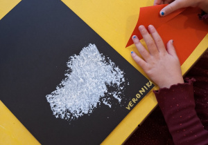 Dziewczynka składa czapkę Mikołaja z czerwonego kartonu.