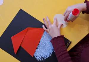 Dziewczynka smaruje klejem papierowy nos Mikołaja.