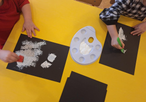 Dzieci malują białą farbą brodę Mikołaja za pomocą gąbki i plastikowego widelca.