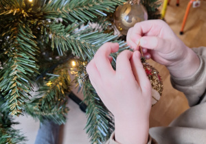 Dziecko zawiesza bombkę na choince.