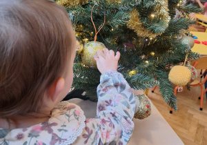 Dziewczynka ogląda złotą bombkę na choince.