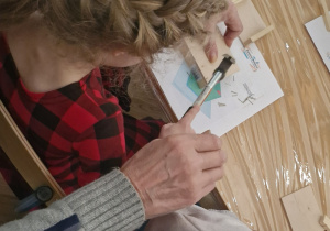 Dziewczynka wspólnie z dziadkiem wbija gwoździki w drewniane podkładki