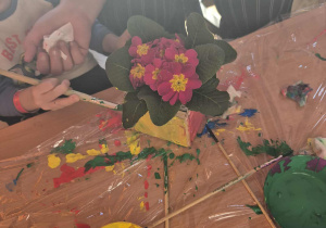 Dziecko z babcią maluje doniczkę, w której posadzony jest kwiatek