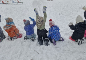 Dzieci siedzą na śniegu i podsypują go w górę.