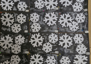 Praca plastyczna - krystaliczne i błyszczące śnieżynki - wiszące na tablicy.