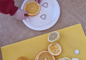 Dziewczynka kładzie plasterek pomarańczy na papierowym talerzyku.