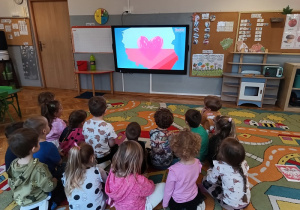 Dzieci oglądają na tablicy multimedialnej film edukacyjny o niepodległości.