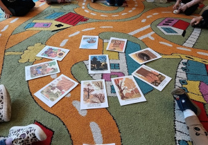 Dzieci siedzą w kole na dywanie, na środku leżą obrazki, przedstawiające zmiany zachodzące w przyrodzie późną jesienią.