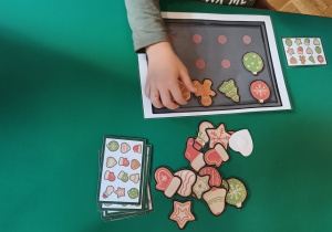 Dziecko przykleja papierowe pierniki na papierową blaszkę według kodu