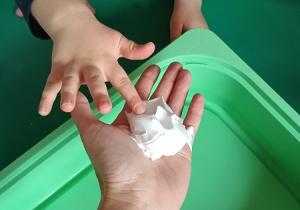 Dziecko dotyka wyciśniętej na rękę nauczyciela pianki do golenia.