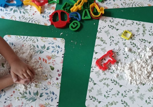 Dzieci bawią się sztucznym śniegiem – ugniatają go, odbijają w nim plastikowe foremki.