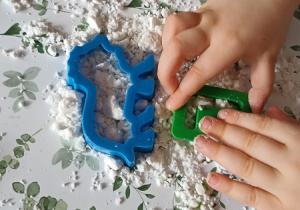 Dziecko odciska kształty z plastikowych foremek na sztucznym śniegu.