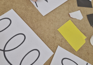 Dzieci pracują przy stoliku - wyklejają szlaczki kawałami wydartego papieru.