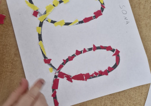 Dziecko wykleja wzór z wykorzystaniem czerwonych i żółtych kawałków papieru.