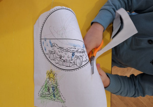 Dziecko wycina nożyczkami bombkę.