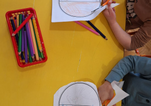 Dzieci wycinają kolorowe bombki nożyczkami.