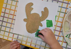 Dziecko stempluje gąbką na kartce zieloną farbą.