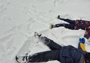 Dzieci robią orzełki na śniegu.