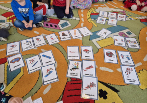 Dzieci siedzą w kole i dopasowują atrybuty pasujące do przedstawionych na obrazkach dyscyplin sportowych.