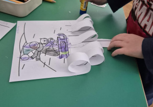 Dziecko wykonuje pracę plastyczną - sanki na śniegu.