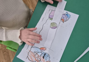 Dziecko przesuwa papierowy pasek imitując rzuty śnieżką od bałwanka do bałwanka.