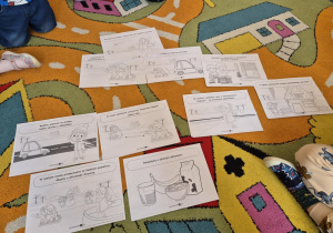 Dzieci siedzą w kole. Na dywanie rozłożone ilustracje przedstawiające zasady bezpiecznych zabaw na śniegu.