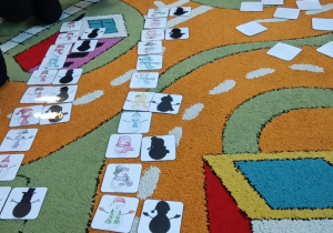 Dzieci w kole na dywanie dopasowują cienie do obrazków bałwanków.