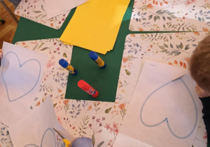 Dzieci przy stolikach wycinają nożyczkami  serca.